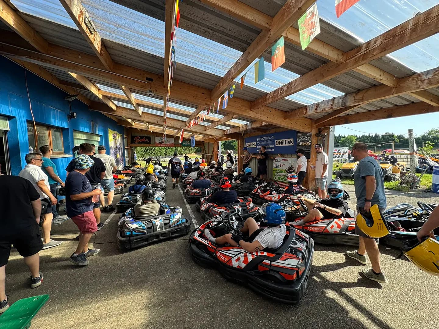 Karts und Fahrer im überdachten Boxenbereich beim Baumafia-Go-Kart-Rennen im Sundgau