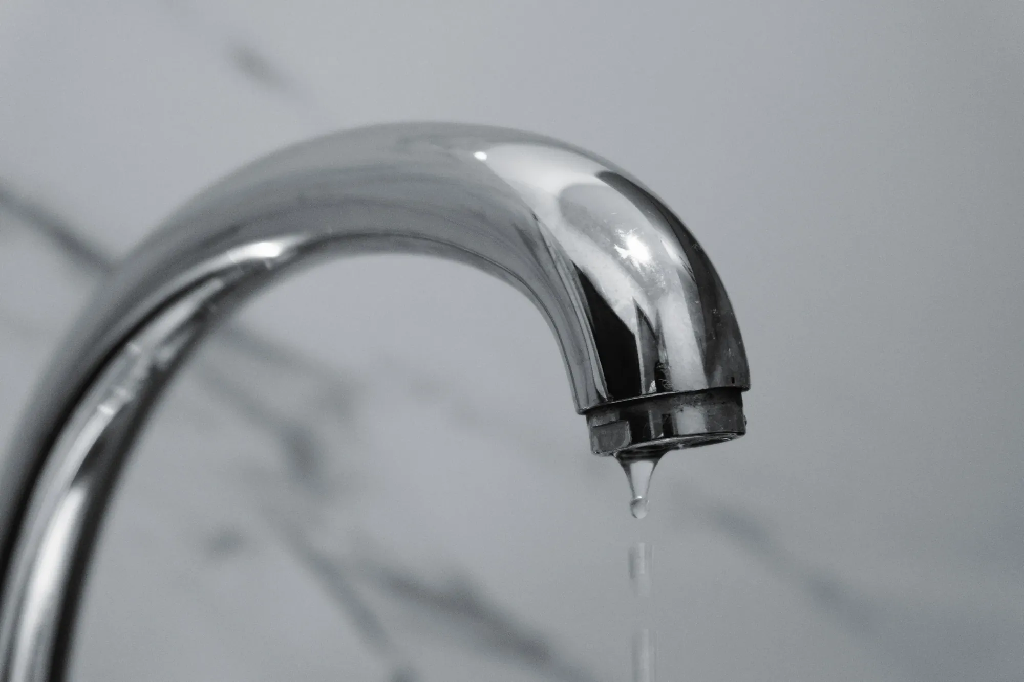 Verchromte Armatur mit Wasserstrahl vor hellem Marmor