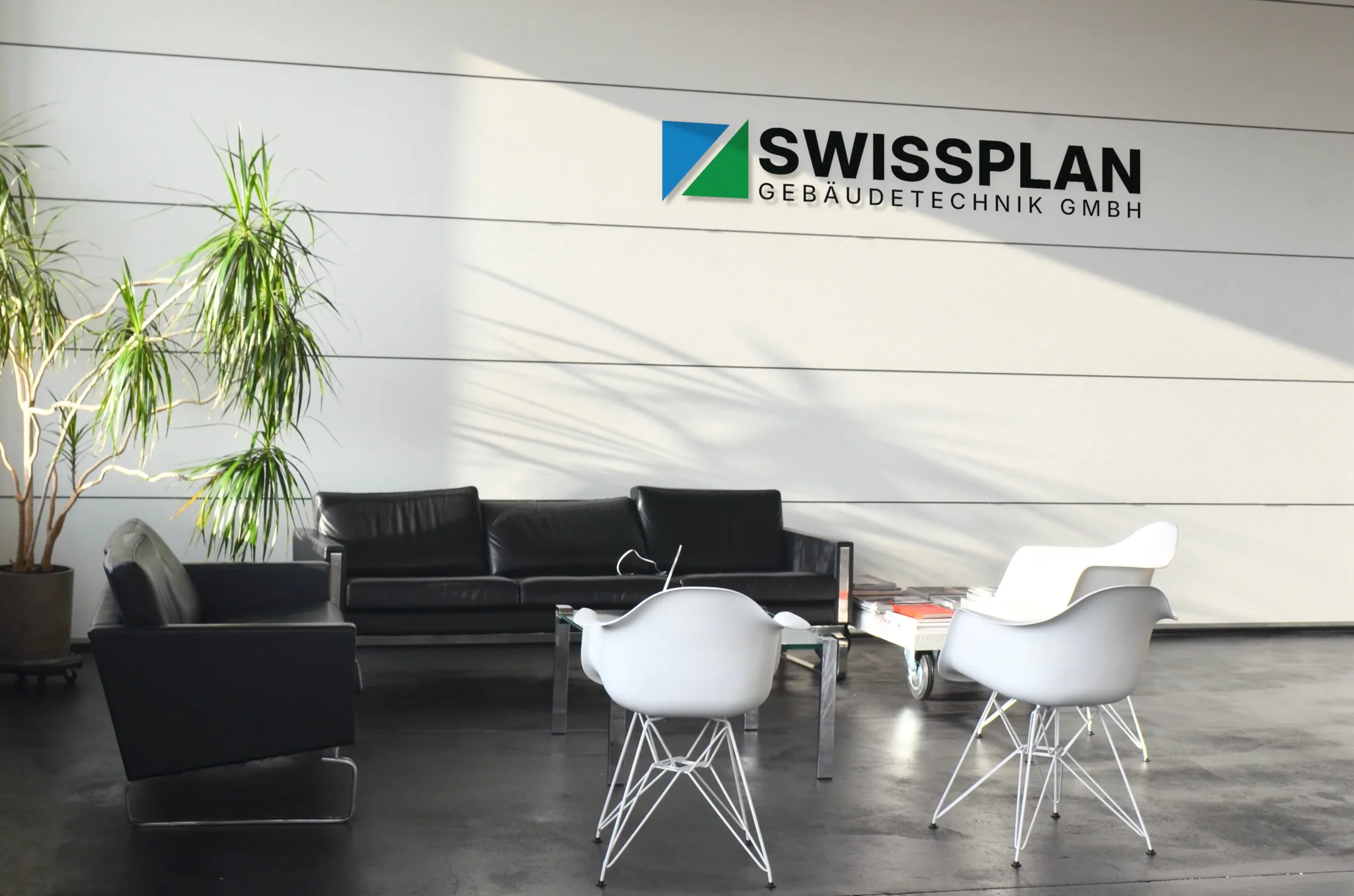 Helle Lobby mit Sofa und Sesseln, an der Wand das Logo von SwissPlan Gebäudetechnik