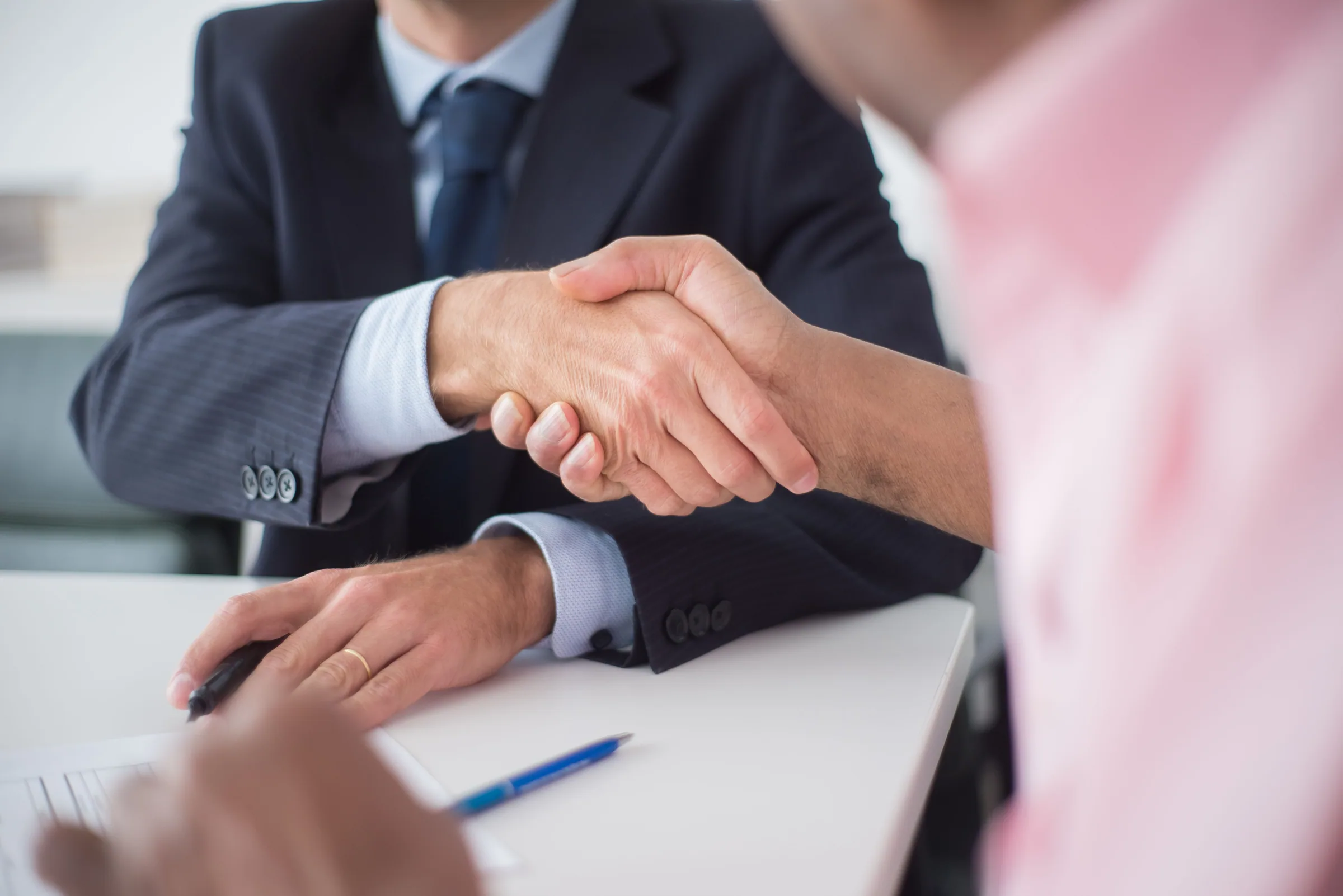 Handschlag über einem Besprechungstisch mit Unterlagen und Kugelschreiber