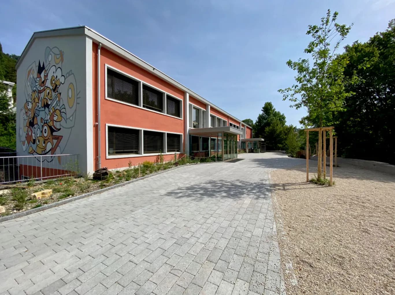 Primarschule Grellingen nach Sanierung und Neubau, Fassade mit Wandbild und Vorplatz